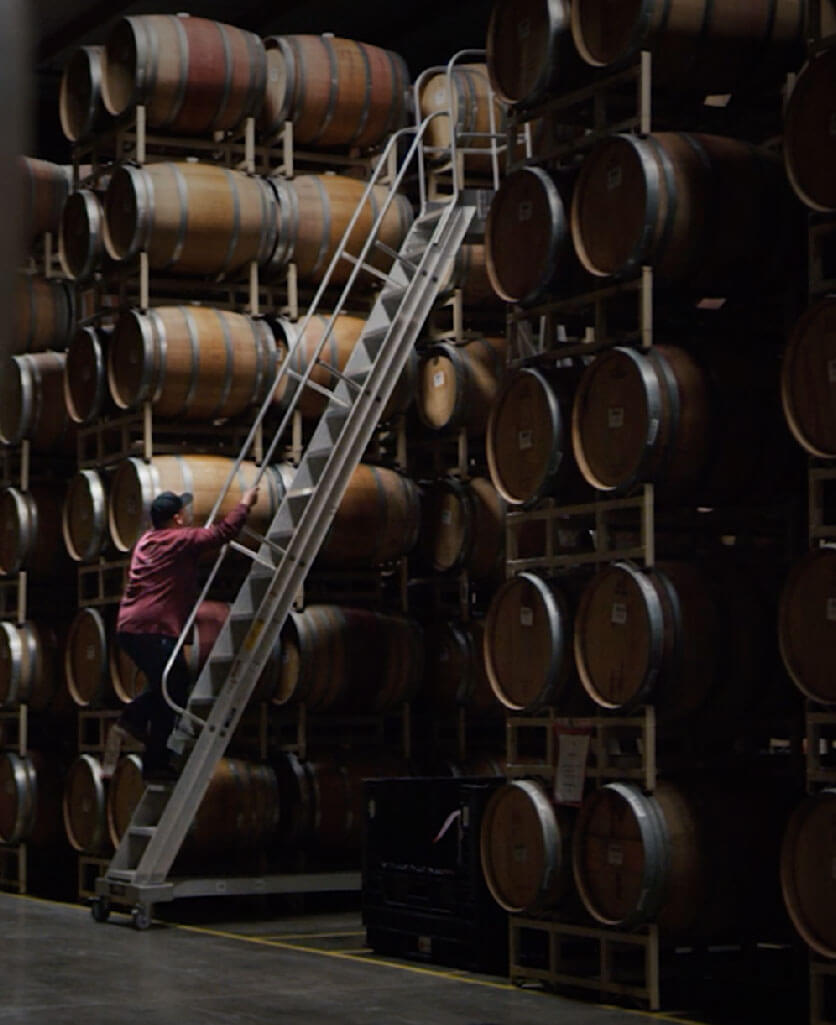man climbing a ladder in a warehouse full of barrels