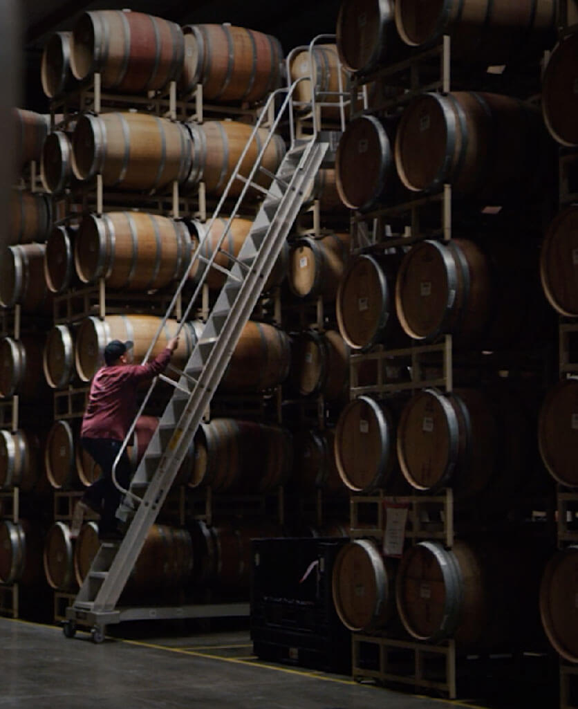 man climbing a ladder in a warehouse full of barrels 